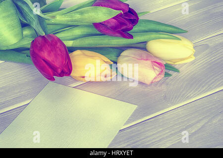 I tulipani bouquet e biglietto di auguri su sfondo di legno. Vintage tonica Foto Stock