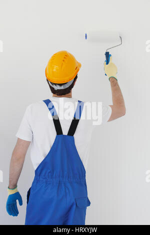 Lavoratore in tuta e uniforme di compressori hardhat dipinto la parete con rullo di vernice Foto Stock