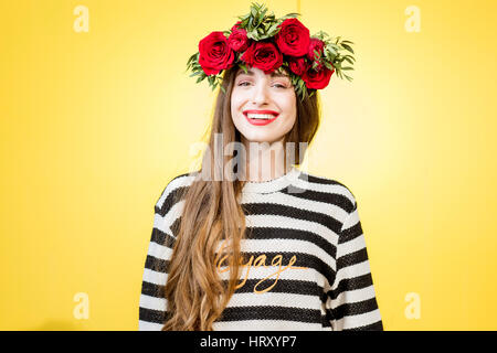 Colorato ritratto di una bella donna in felpa con ghirlanda fatta di rose rosse su sfondo giallo Foto Stock