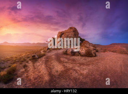 Deserto con rocce solitarie contro multicolore di cielo nuvoloso al tramonto. Blu, Viola e rosso nuvole. Panoramica. Paesaggio colorato con il sentiero, pietre Foto Stock