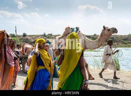 Un cammello ed è herder croce di fronte due luminosamente donna adornata a Baneshwar Mela Foto Stock