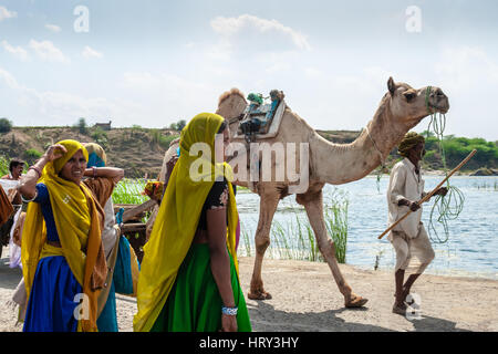 Un cammello ed è herder croce di fronte due luminosamente donna adornata a Baneshwar Mela Foto Stock