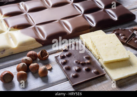 Pezzi di piastrella cioccolatini, i dadi e le fave di cacao su sfondo di legno Foto Stock