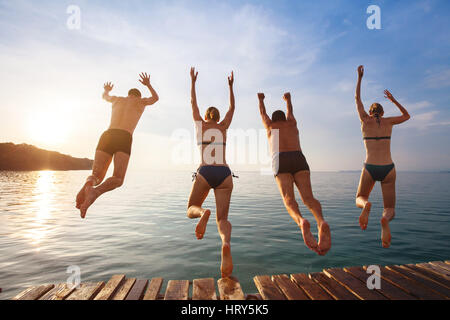 Gruppo di amici jumping al mare dal molo, felici vacanze in spiaggia Foto Stock