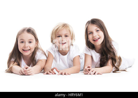 Sorridenti tre bambini in bianche vesti la posa sul pavimento isolato su sfondo bianco Foto Stock