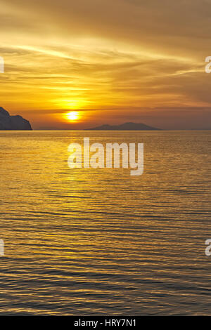 Tramonto sulla spiaggia con belle drammatico giallo e arancione del cielo. Silhouette di un'isola molto più avanti in vista. Foto Stock