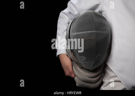 Fencer donna tenere il casco in mano e indossando bianco costume di scherma. Isolato su sfondo nero. Foto Stock