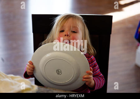 Una bambina di 2 anni di età) leccare la sua piastra dopo la cena Foto Stock