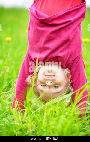 Felice bambina in piedi capovolta su erba in estate park Foto Stock
