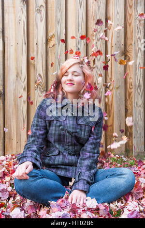 Giovane donna seduta contro il recinto con la caduta di rosso le foglie di autunno sorridente Foto Stock