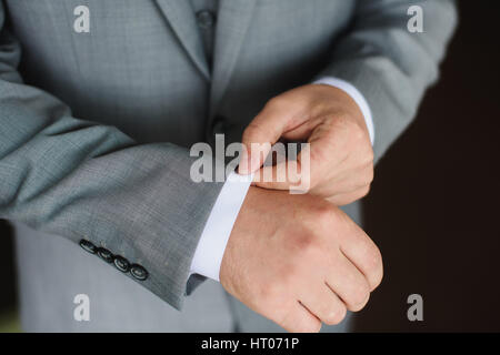 Elegante moda giovane uomo vestirsi per la celebrazione dei matrimoni. Colore close up immagine di mani maschili. Lo sposo abbottonatura una camicia. Sfondo scuro. Foto Stock