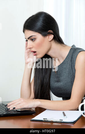 Giovane donna di affari presso il suo ufficio. Guarda il suo laptop sorpreso. Foto Stock