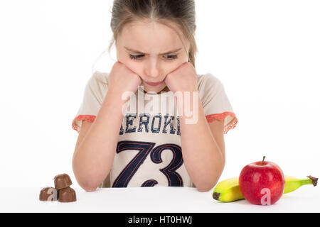 Ragazza di decidere tra dolci e frutta. Isolato. Sfondo bianco. Foto Stock