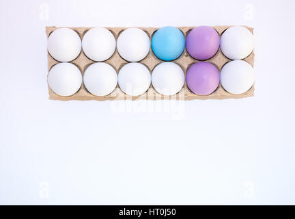 Due uova di Pasqua tinte di giallo, un uovo tinti di blu e bianco di nove di gallina uova in un tan scatola di cartone dal di sopra su sfondo bianco con copia spazio. Foto Stock