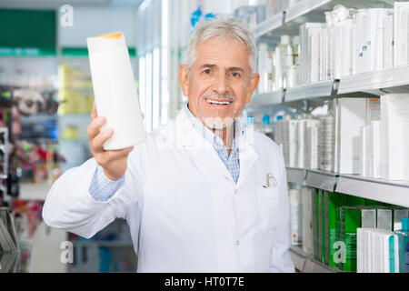 Ritratto di farmacista maschio sorridente tenendo bottiglia di shampoo in farmacia Foto Stock