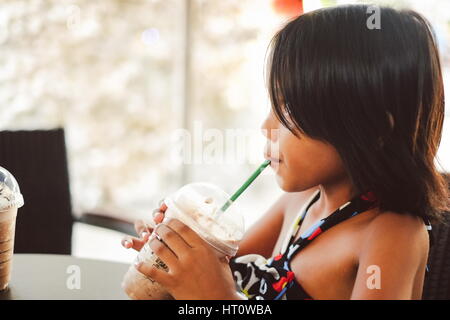 Carino bambina di bere ghiaccio freddo agitare di cioccolato in un cafe Foto Stock