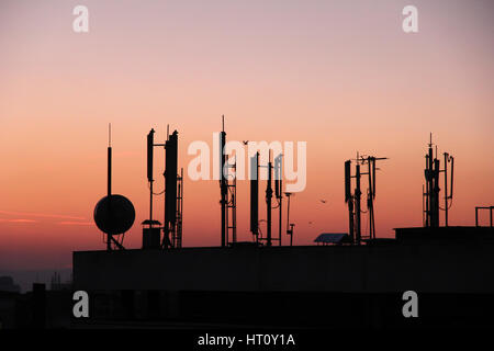 Silhouette di trasmettitori gsm sul tetto edificio per uffici al crepuscolo Foto Stock