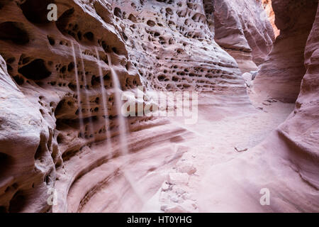 Sabbia collocato in diversi piccoli fori nel lato di una slot canyon riversa al sabbioso del canyon. Una lunga esposizione smussa tutto fuori per un morbido Foto Stock
