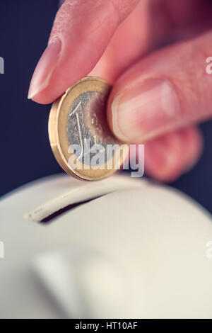 Donna mettendo una moneta in euro nel salvadanaio, risparmio di denaro e di bilancio home concept, macro close up di dita Foto Stock