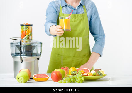 Anonimo donna che indossa un grembiule, offrendo un bicchiere di fresco succo pressato, uno stile di vita sano concetto su sfondo bianco Foto Stock