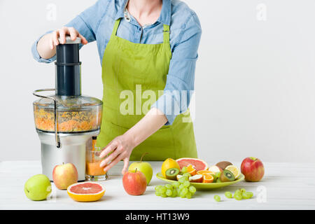 Anonimo donna che indossa un grembiule, la preparazione di un sano succo di frutta utilizzando moderne spremiagrumi elettrico, uno stile di vita sano concetto su sfondo bianco Foto Stock