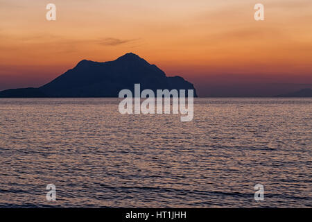 Tramonto sulla spiaggia con belle drammatico giallo e arancione del cielo. Silhouette di un'isola molto più avanti in vista. Foto Stock