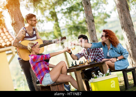 Team di giovani amici brinda con tatuato ragazzo con la chitarra in natura Foto Stock