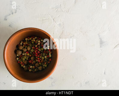 Peperoni multicolori piselli in un vaso di argilla su un sfondo di pietra. Spazio per il testo. Foto Stock