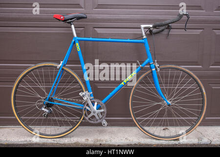 Un vecchio blu Trek bicicletta 300 sistemata con bull manico in corno di barre appoggia contro un marrone porta di garage. Foto Stock