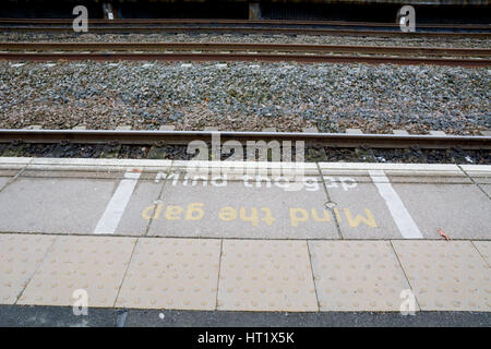 Dipinto si prega di mente il divario segno sulla stazione ferroviaria platform Foto Stock