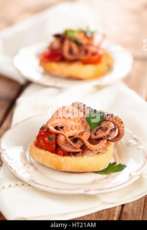 Il cibo italiano. Bruschetta con polipetti, pomodori e prezzemolo. Foto Stock