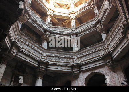 Piani superiori con intricati intarsi in pietra su pilastri, lesena e trabeazione. Adalaj Stepwell, Ahmedabad, Gujarat, India. Foto Stock