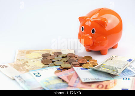 Salvadanaio guardando una pila di banconote e monete in euro. Foto Stock