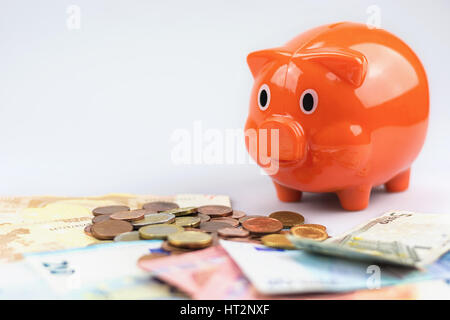 Salvadanaio guardando una pila di banconote e monete in euro. Foto Stock