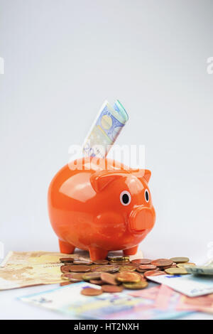 Salvadanaio guardando una pila di banconote e monete in euro. Foto Stock