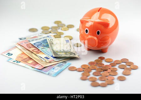 Salvadanaio guardando una pila di banconote e monete in euro. Foto Stock