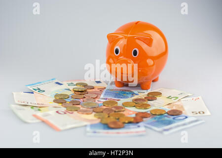 Salvadanaio guardando una pila di banconote e monete in euro. Foto Stock