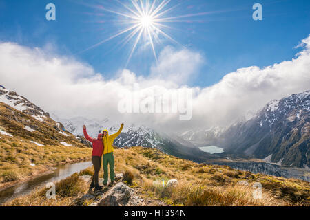 Due escursionisti che si allunga braccia, vista sulla valle di Hooker, lago di montagna Sealy Tarns, parco nazionale di Mount Cook, regione di Canterbury Foto Stock