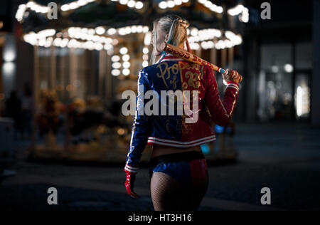 Cosplayer ragazza in costume Harley Quinn sullo sfondo luci della città di notte. Vista posteriore. Cosplay Foto Stock