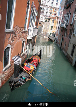 Esplora gli stretti canali veneziani in una tradizionale gondola con gondoliere durante una giornata di sole a Venezia. Italia Foto Stock