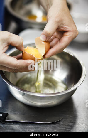 Lo chef si rompe l'uovo in una coppa in acciaio su cucina professionale Foto Stock