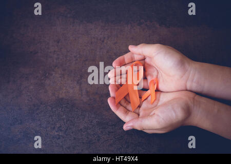 Mani che tengono i nastri di colore arancione su sfondo tonificante, leucemia consapevolezza, di per sé pregiudizio Giornata di sensibilizzazione, sclerosi multipla consapevolezza, cancro del rene awarenes Foto Stock