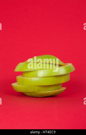 Fette di mela verde su uno sfondo di colore rosso. Foto Stock