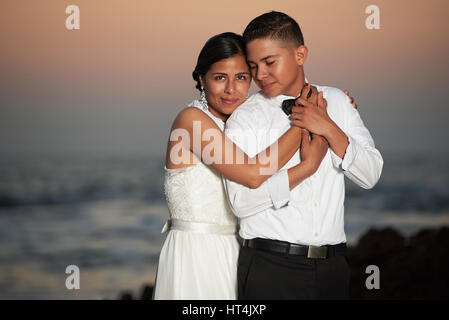 Ispanico sposa e lo sposo ritratto su arancione tramonto sfondo con copia spazio. I giovani sposi abbraccio Foto Stock