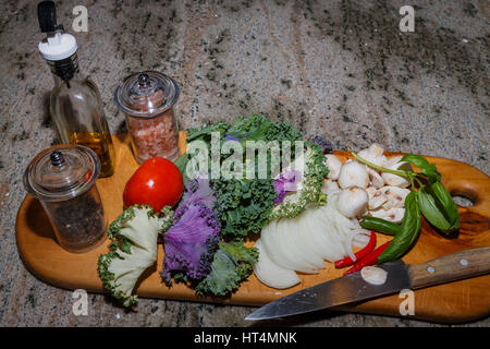 Preparazione per un insalata di pomodoro, lettuge, la cipolla, i funghi peperoncini e erbe aromatiche fresche con olio di oliva e sale e pepe per la stagionatura. Tutti su un taglio Foto Stock