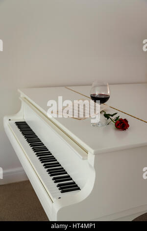 Un pianoforte a coda con una rosa rossa e un bicchiere di vino rosso pronto per una celebrazione.Il tempo di partito. Foto Stock