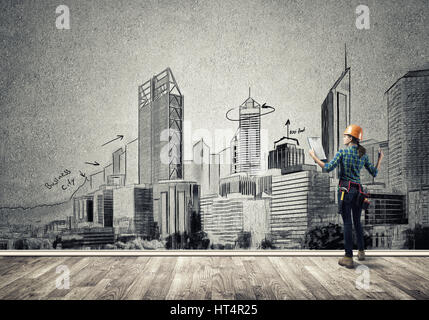 Vista posteriore di ingegnere di donna con la cartella e schizzi di progetto di costruzione sulla parete Foto Stock