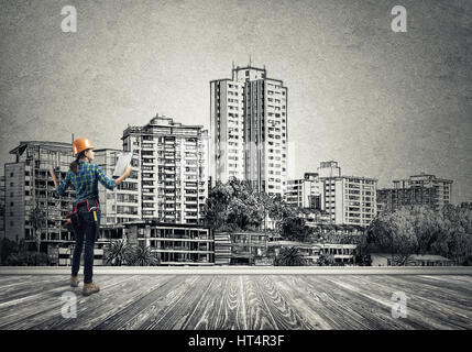 Vista posteriore di ingegnere di donna con la cartella e schizzi di progetto di costruzione sulla parete Foto Stock