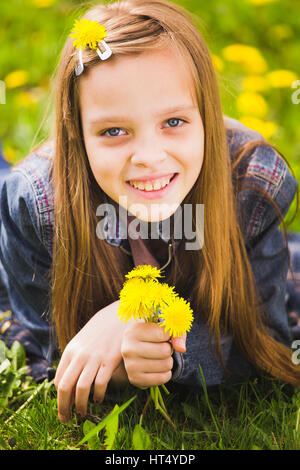 Ritratto di primavera ragazza. Primo piano della giovane e bella ragazza sorridente con bouquet di giallo di tarassaco in mani isolate su erba verde dello sfondo. Età di Foto Stock