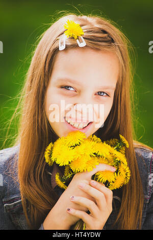 Ritratto di primavera ragazza. Primo piano della giovane e bella ragazza sorridente con bouquet di giallo di tarassaco in mani isolate su erba verde dello sfondo. Età di Foto Stock